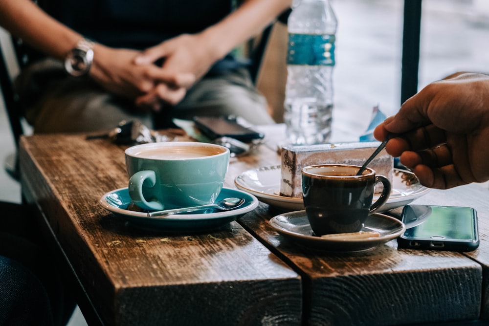 person holding blue ceramic mug on blue ceramic saucer