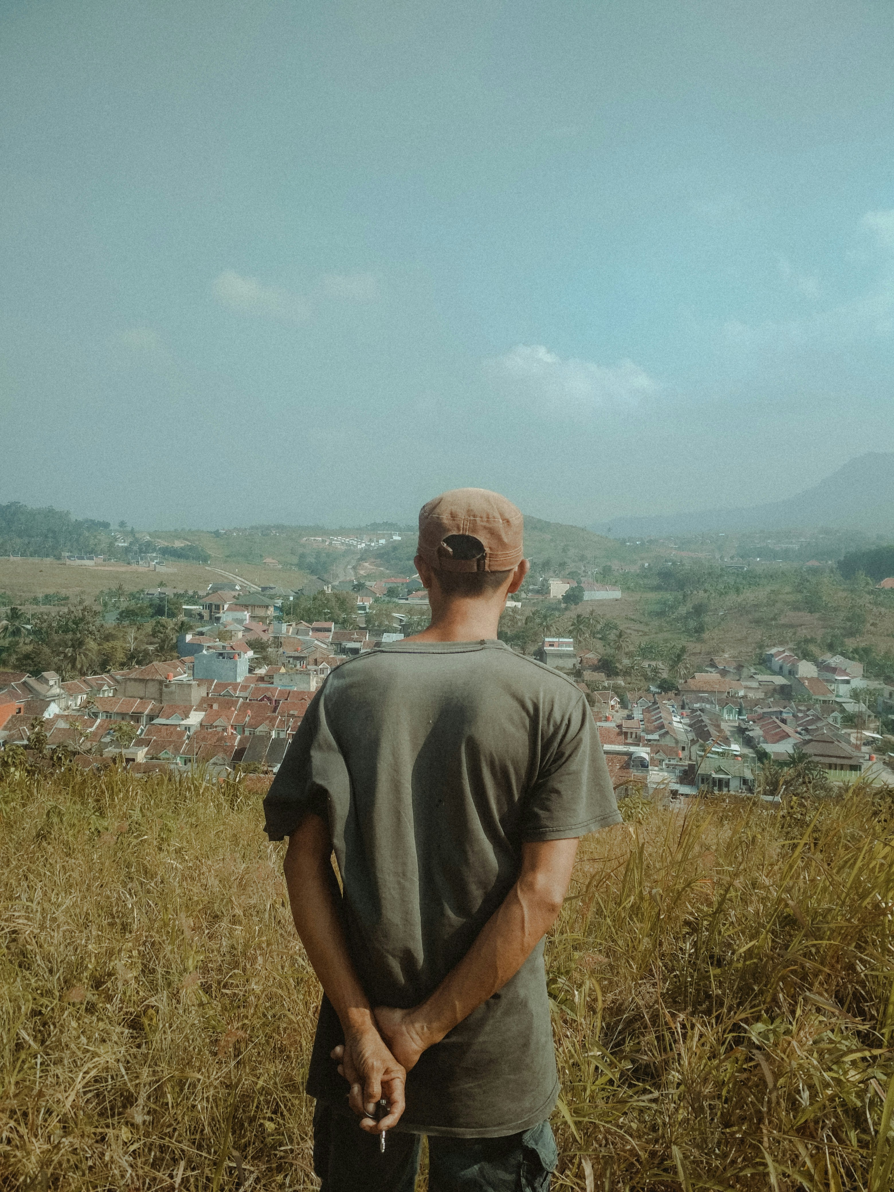 Pria dengan kaos leher kru abu-abu berdiri di lapangan rumput hijau di siang hari