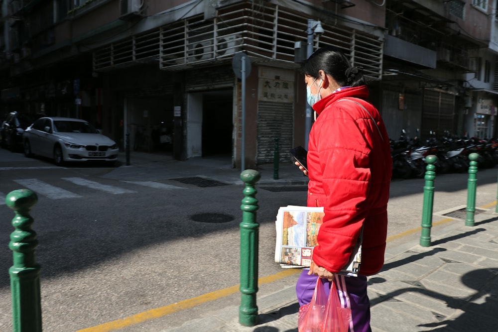 man in red jacket and black pants walking on sidewalk during daytime