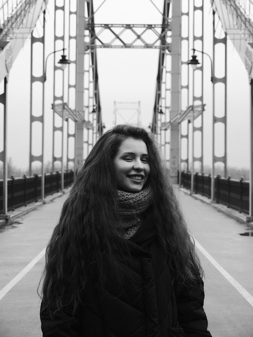 grayscale photo of woman in black coat standing on sidewalk