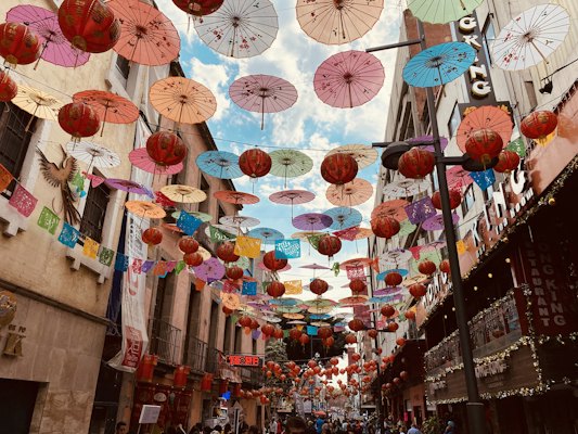 Colorful paper umbrellas and red lanterns hanging above a narrow street in Mexico City