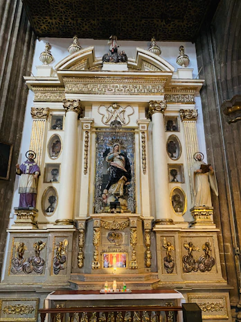 A serene altar setup featuring candles, a statue of a saint, and elegant religious artifacts.