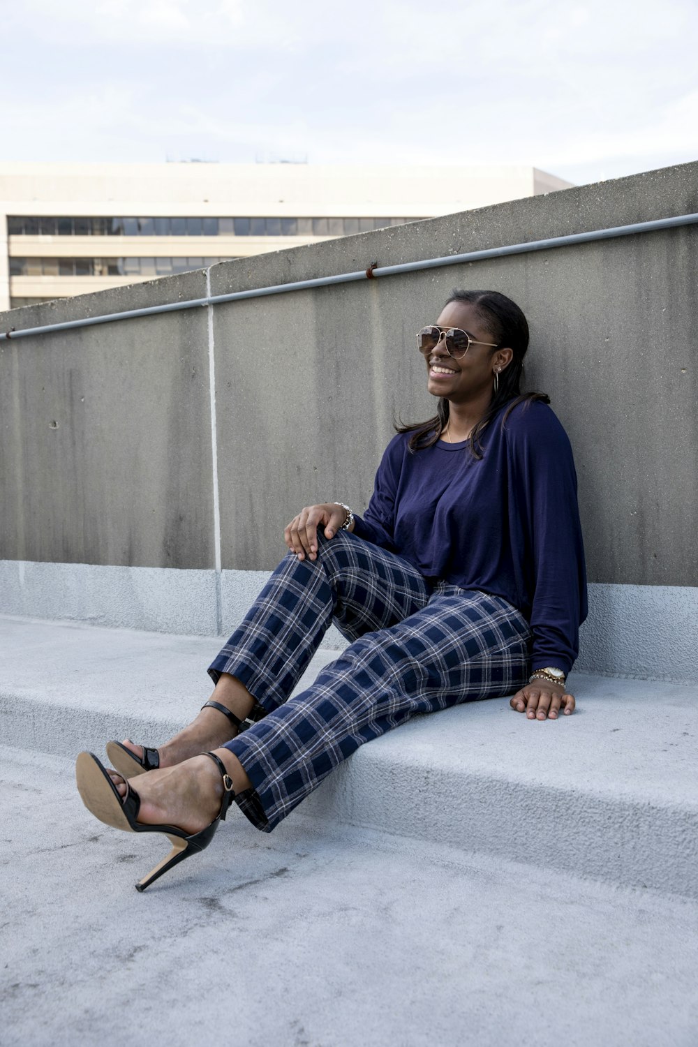 woman in blue long sleeve shirt and black white plaid pants sitting on gray concrete floor