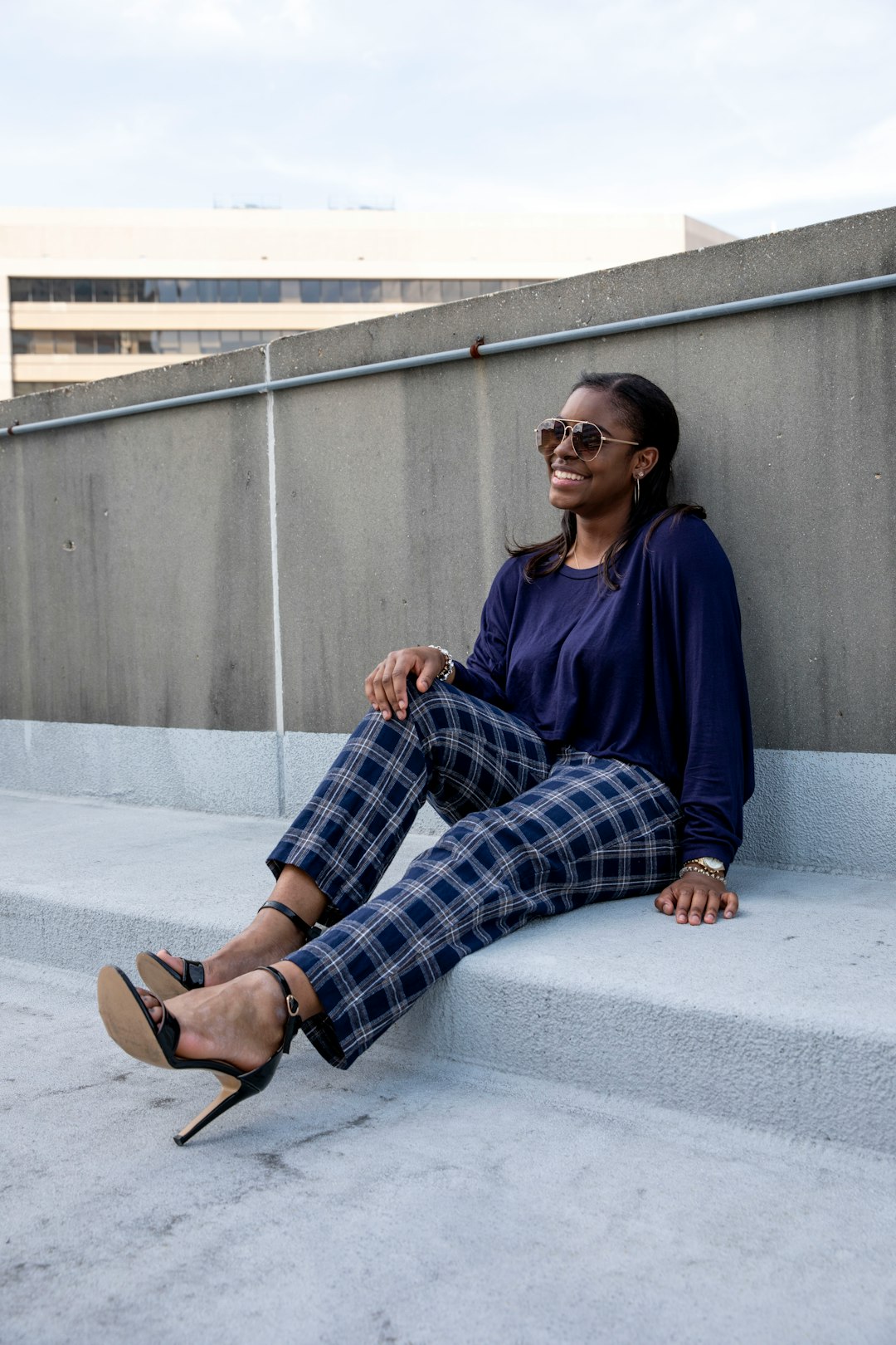 woman in blue long sleeve shirt and black white plaid pants sitting on gray concrete floor