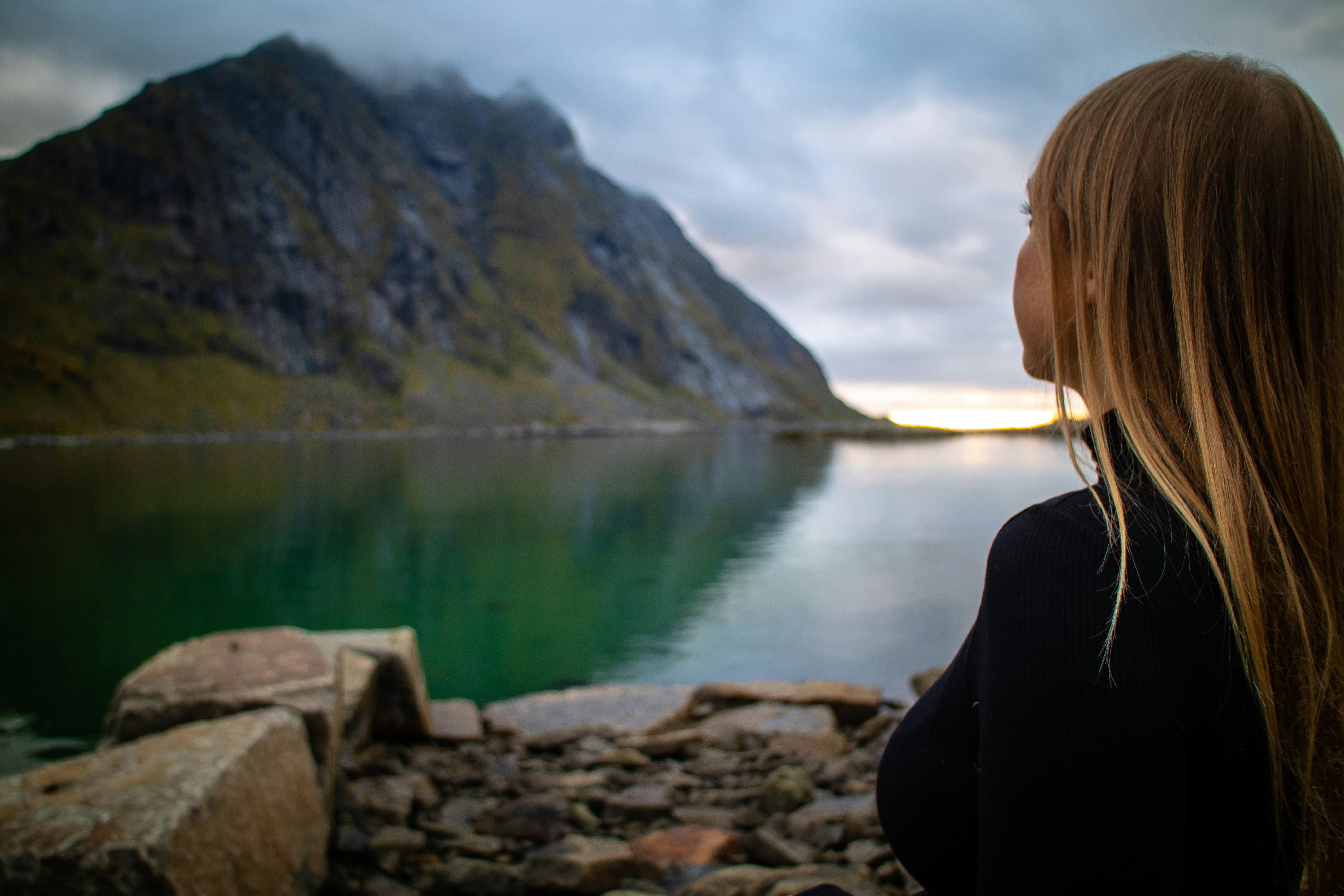 woman in black jacket sitting on rock near lake during daytime