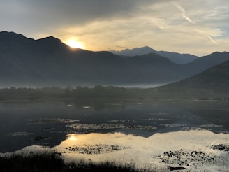 A serene landscape featuring a calm lake surrounded by mountains at sunset.