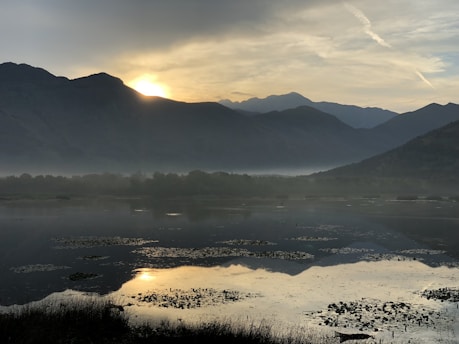A serene landscape featuring a calm lake surrounded by mountains at sunset.
