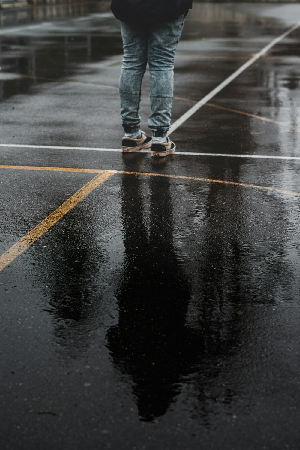 person in blue denim jeans and brown shoes standing on black asphalt road