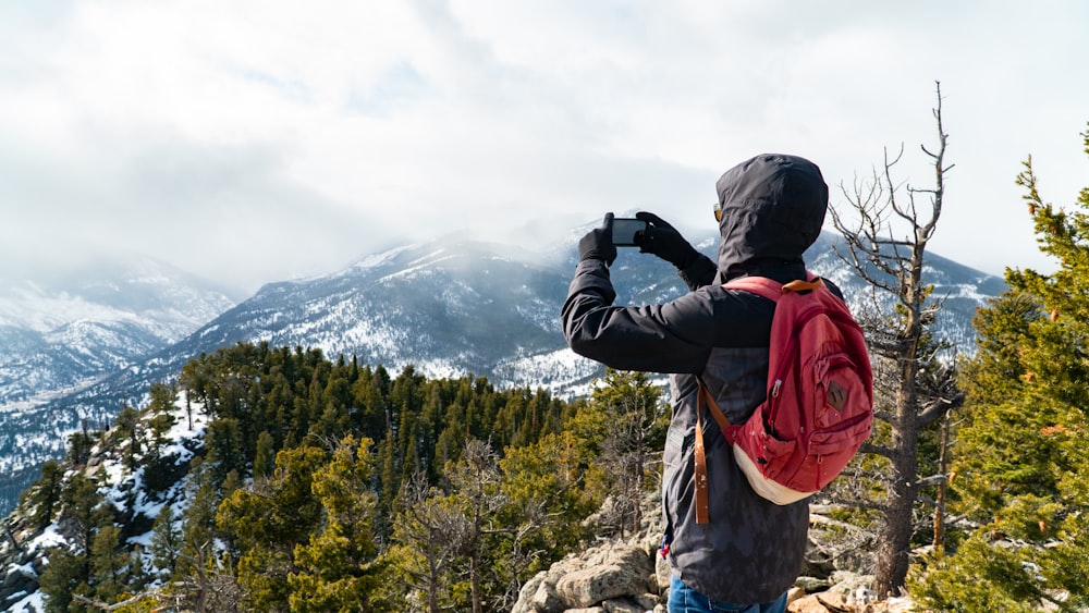 man in black jacket and orange backpack standing on rock formation during daytime