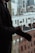 A person in a suit is putting on a glove while standing near a window overlooking a cityscape with tall buildings. The image reflects a professional setting.