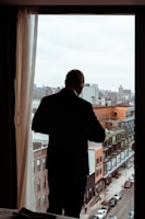 man in black dress shirt standing near window during daytime