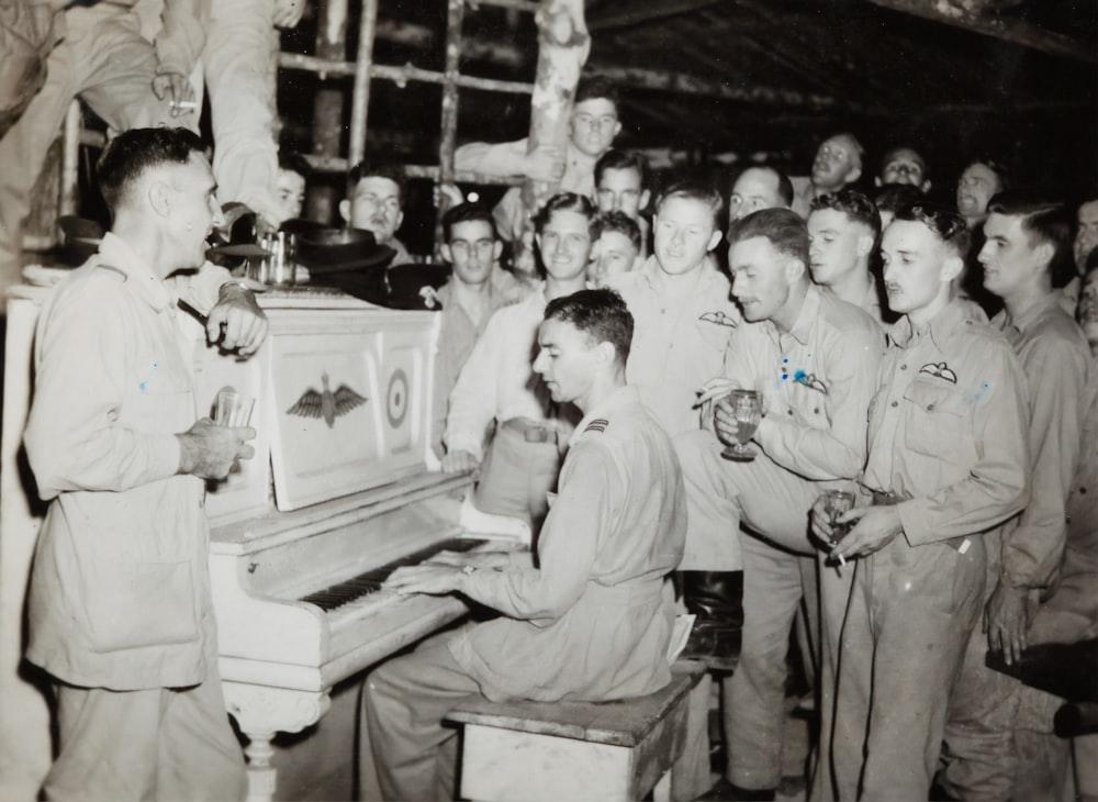 foto em tons de cinza de 4 homens em pé ao lado do piano