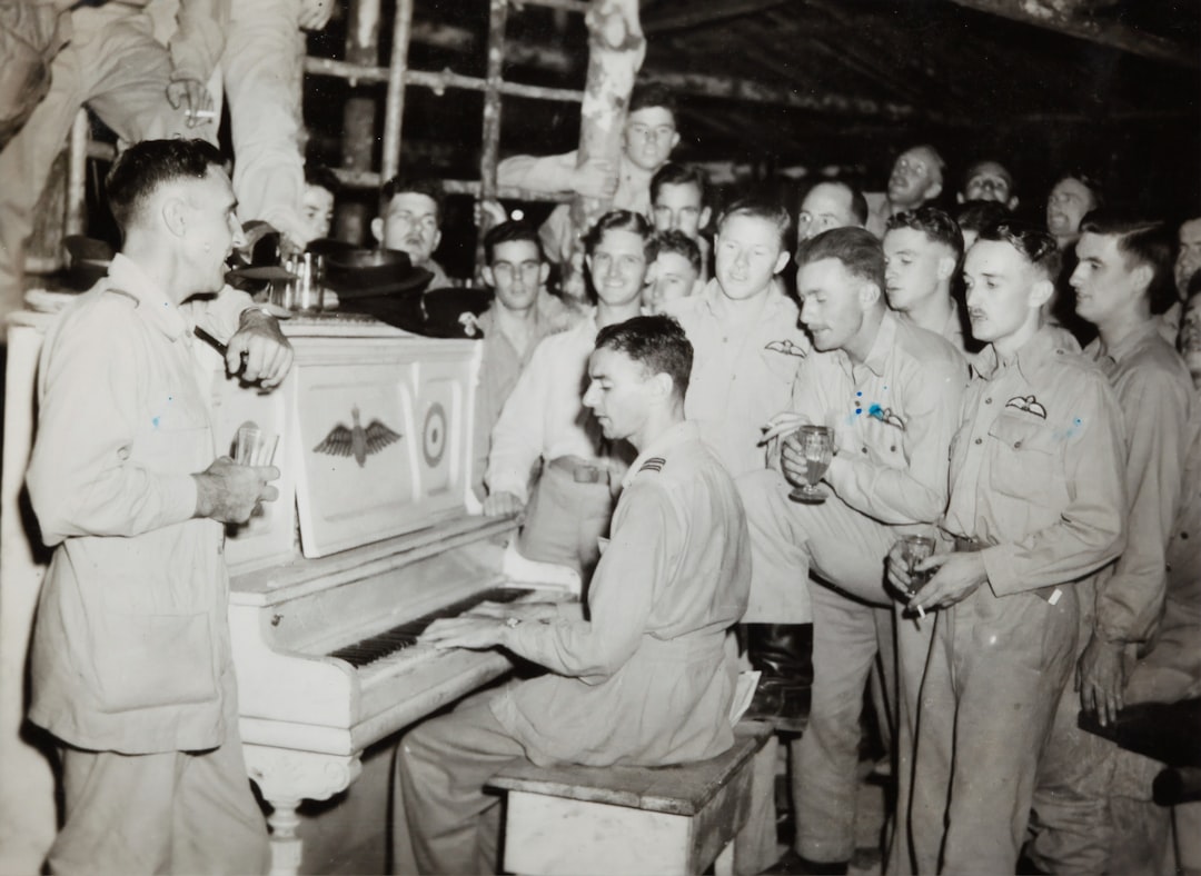 grayscale photo of 4 men standing beside piano,