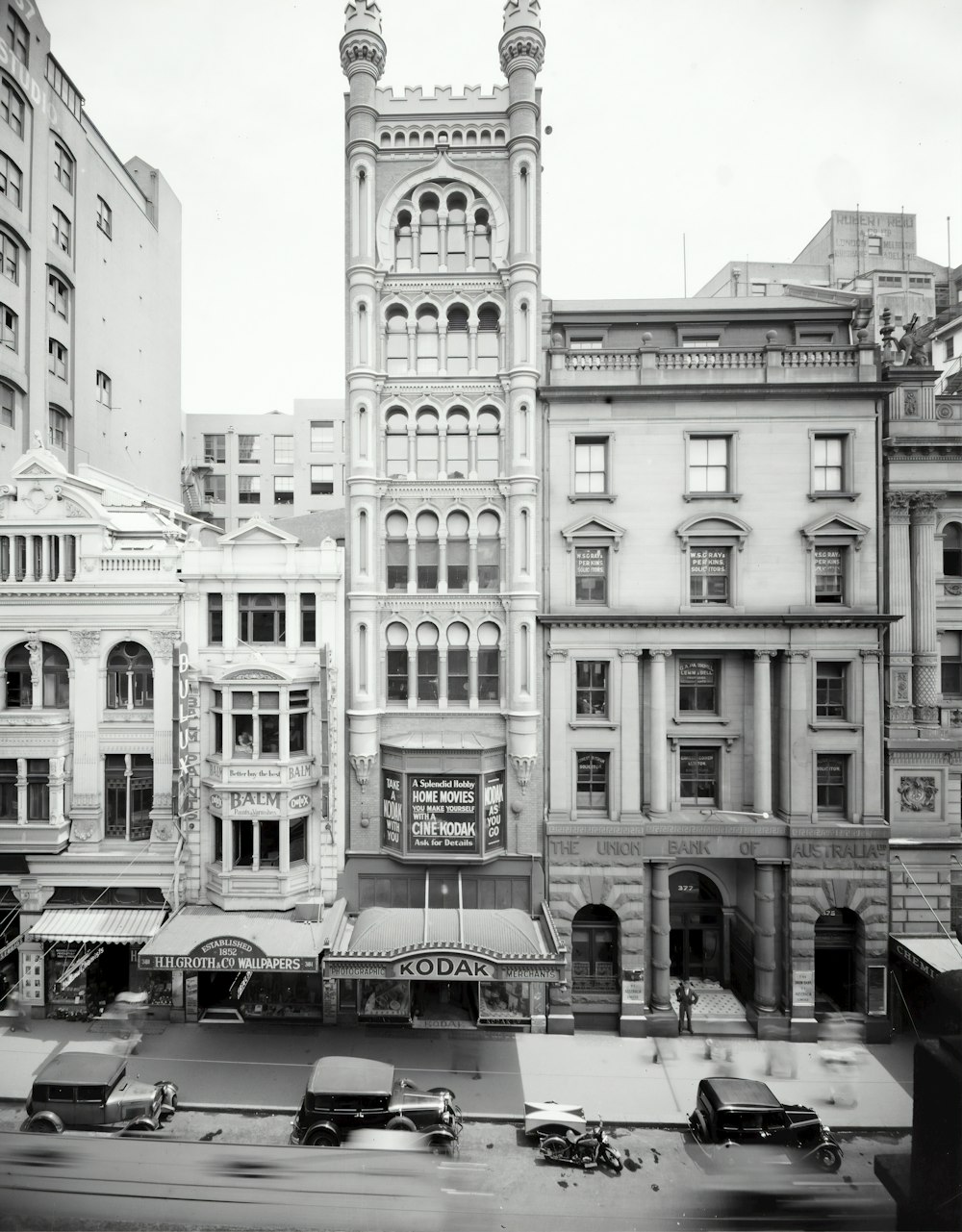 grayscale photo of people walking on sidewalk near building