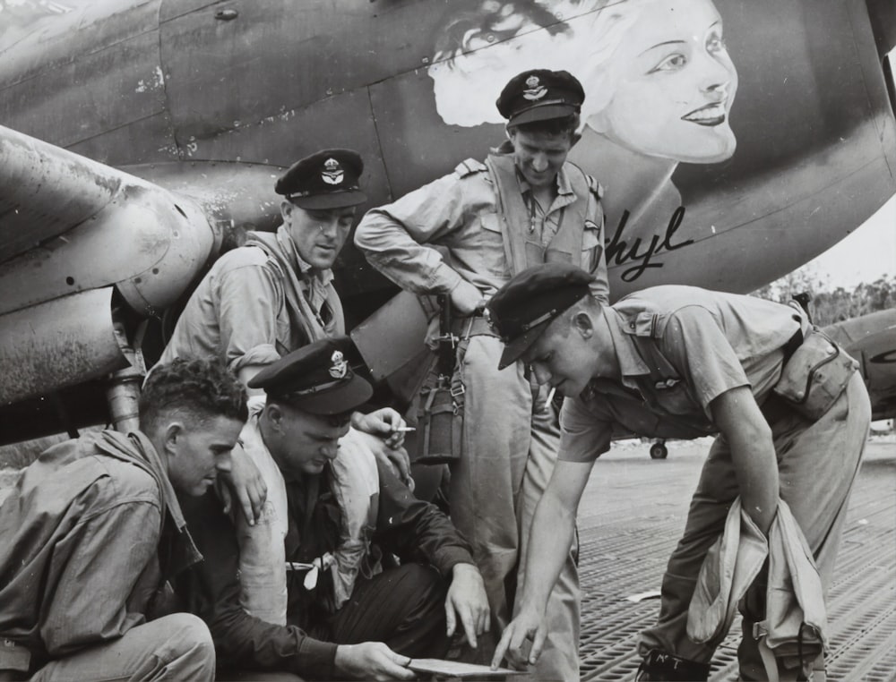 grayscale photo of men in uniform sitting on concrete wall