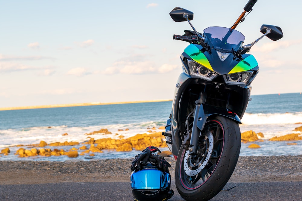 blue and black sports bike on gray sand near body of water during daytime