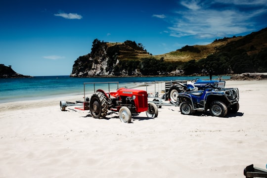 red tractor on beach during daytime in Hahei New Zealand