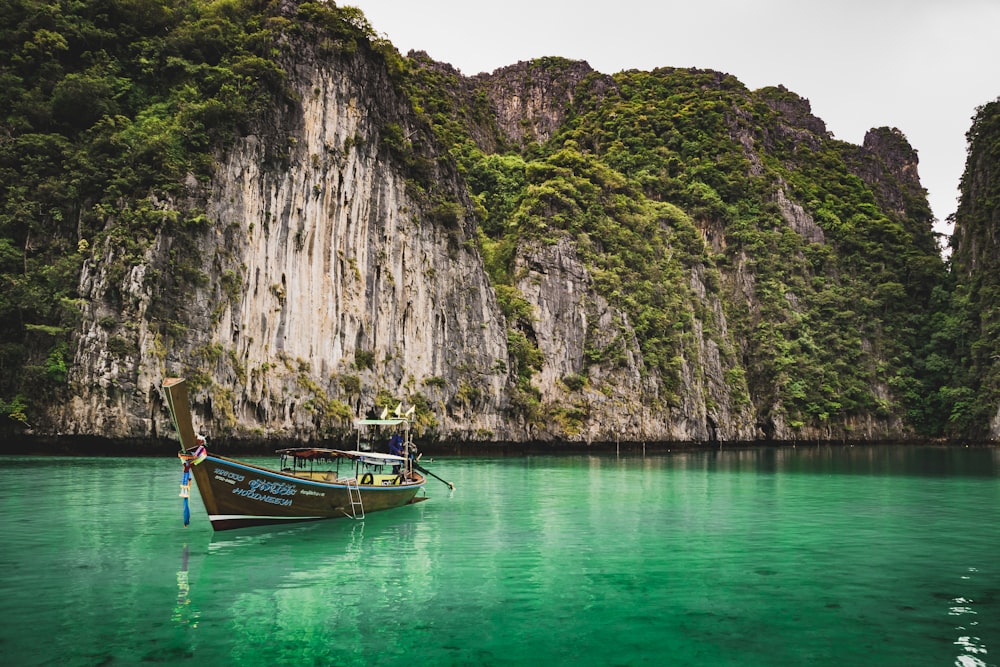 brown boat on body of water near mountain during daytime