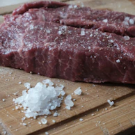 Close-up of a juicy steak resting on a wooden board with herbs and coarse salt sprinkled around.
