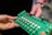 Two hands are holding a green electronic circuit board. The board contains various components such as capacitors, resistors, and connectors, with a label that reads 'LettUS Grow'. It appears to be part of an electronic device or system.