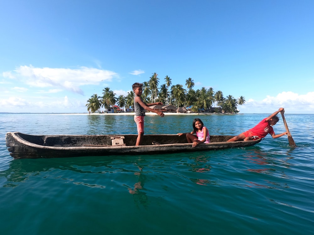 赤と黒のビキニを着た3人の女性が、日中に水面に浮かぶ茶色のボートに乗っている