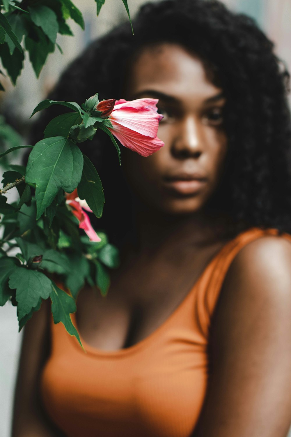 woman in orange tank top holding red hibiscus