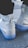 A pair of white Nike Air shoes with Gore-Tex branding is shown from the back. The shoes have a chunky sole with a translucent blue tint and a high-top design. They are being worn with white socks, and the surface beneath is a textured gray pavement.