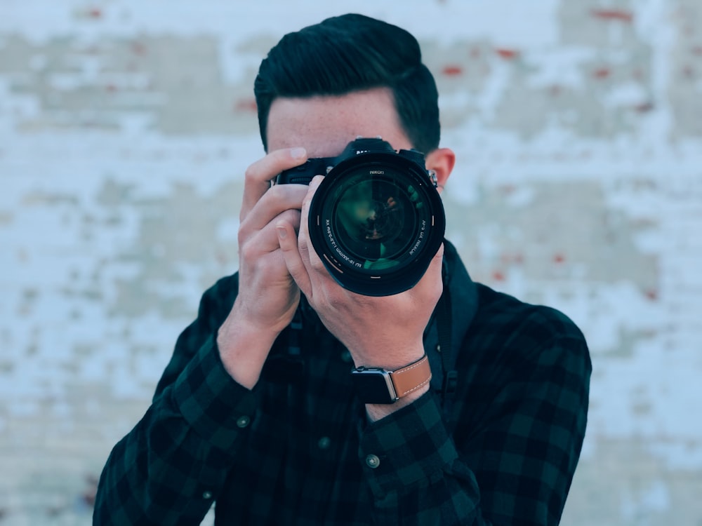 man in blue and black plaid dress shirt holding black dslr camera