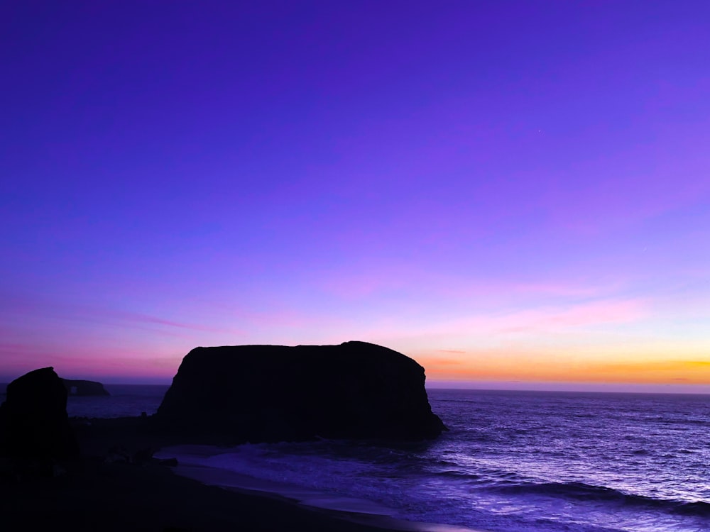 silhouette of rock formation on sea during sunset