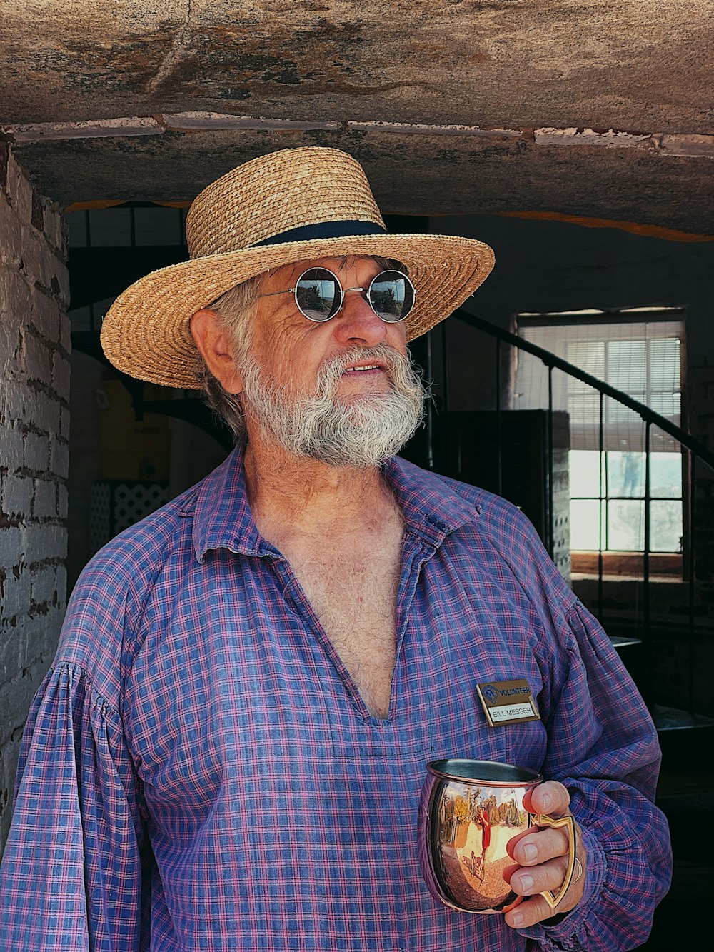 man in blue and white plaid button up shirt wearing brown straw hat holding clear drinking
