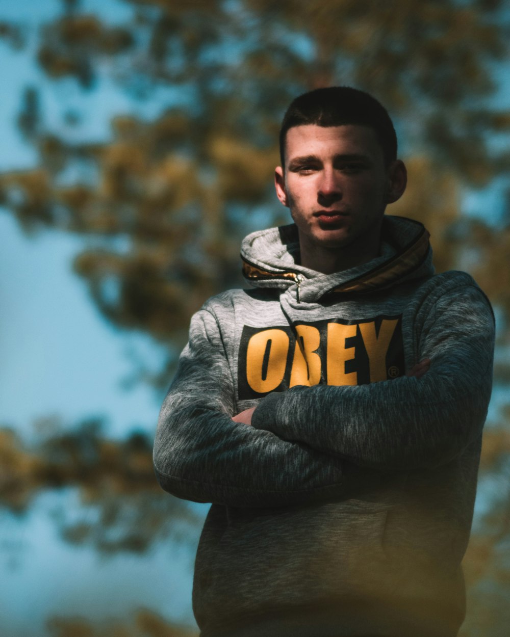 man in gray and yellow hoodie standing near brown trees during daytime