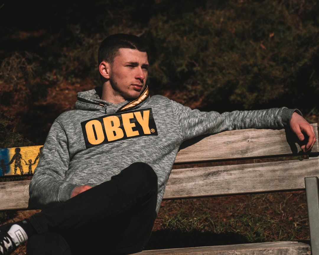 man in gray and black hoodie and black pants sitting on brown wooden bench