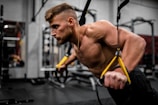 topless man in black pants holding black and yellow exercise equipment