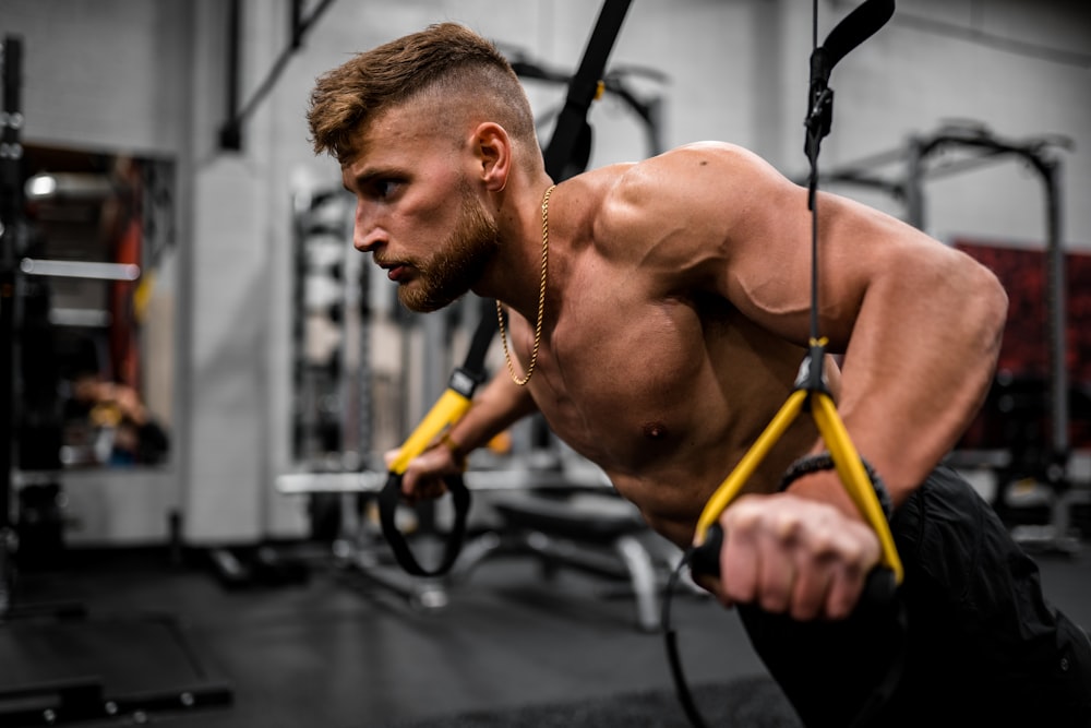 topless man in black pants holding black and yellow exercise equipment