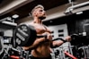 topless man in black shorts carrying black dumbbell