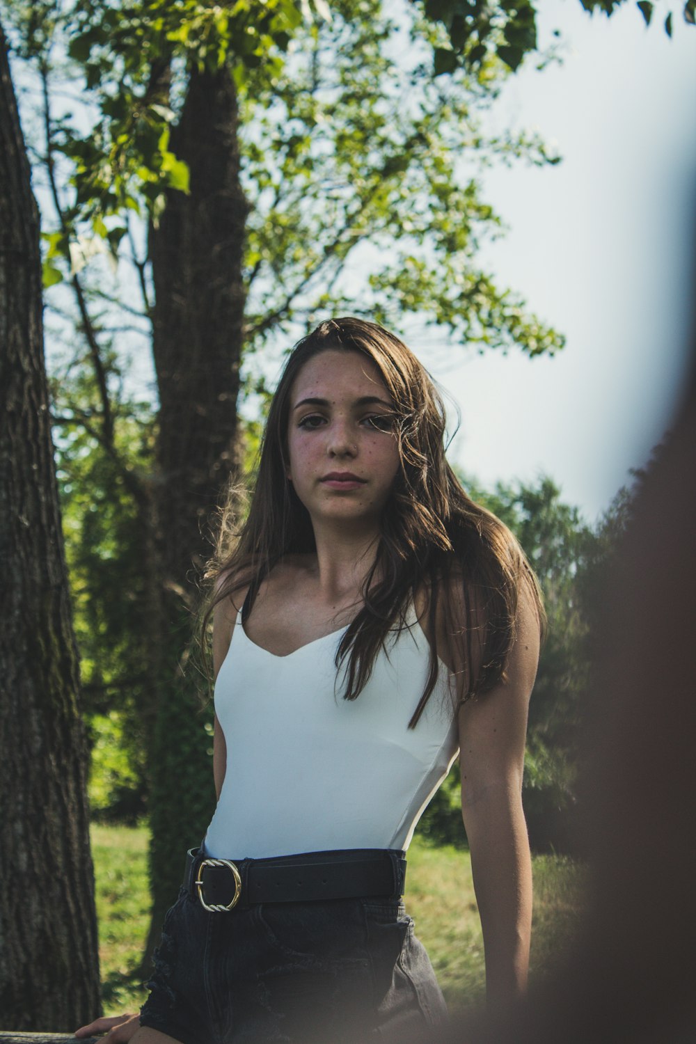 woman in white tank top standing near trees during daytime