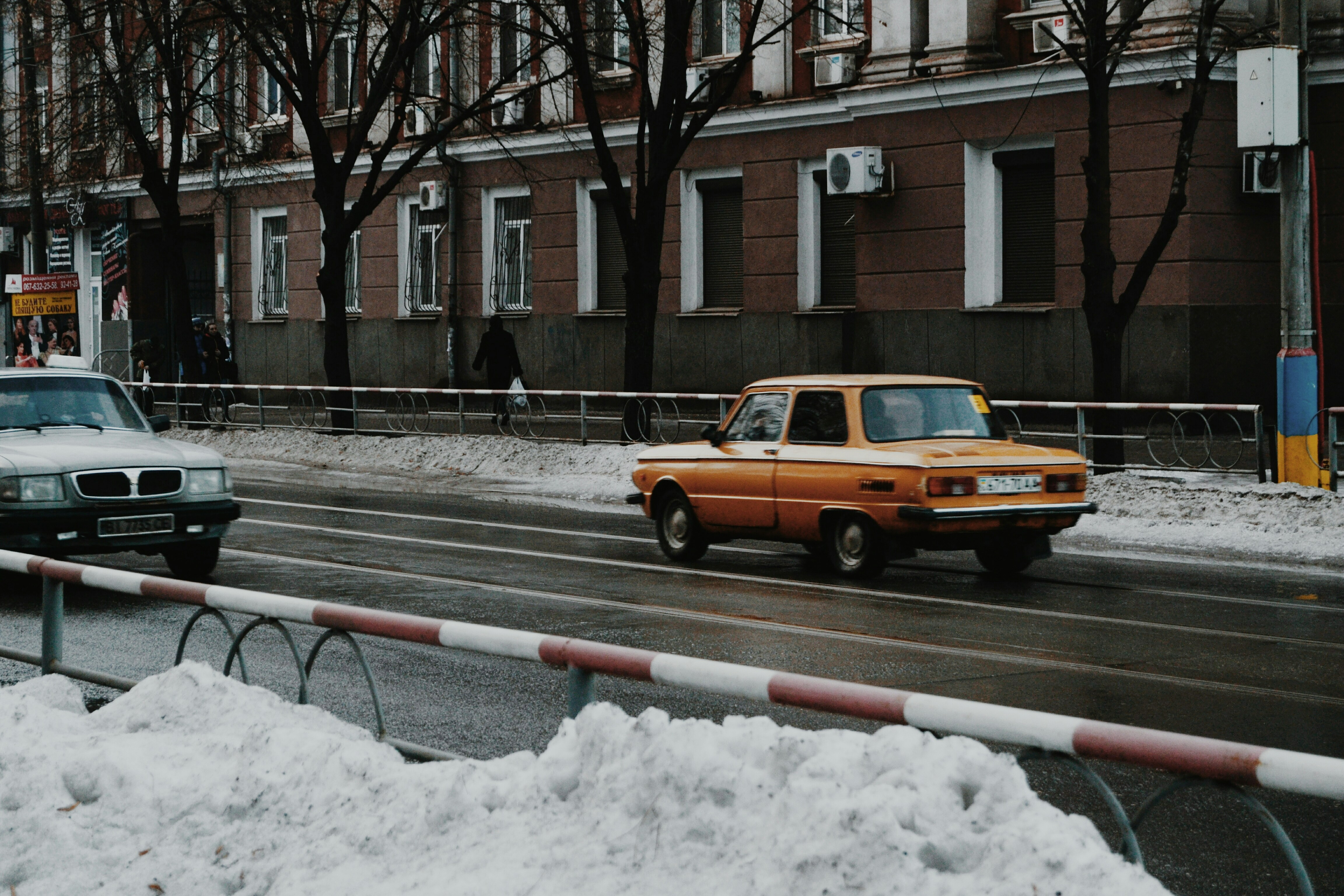 a yellow car driving down a snow covered street