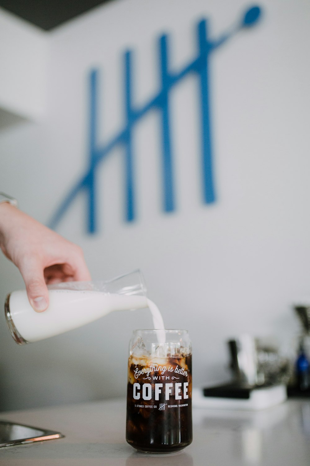 person pouring white liquid on clear drinking glass