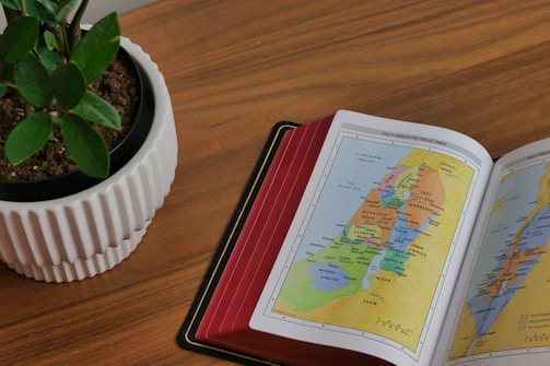 An open book with a map and travel accessories on a wooden table.
