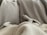 A pair of small dog paws and a tail are visible peeking out from under a cozy blanket. The background consists of multiple blankets in neutral tones such as beige and grey, creating a warm and comfortable setting.