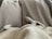 A pair of small dog paws and a tail are visible peeking out from under a cozy blanket. The background consists of multiple blankets in neutral tones such as beige and grey, creating a warm and comfortable setting.