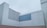A minimalist architectural structure with clean, geometric lines and a modern aesthetic. The building features a stark contrast between light grey and darker grey panels, with a seamless, block-like design. The sky is overcast, adding to the monochromatic theme.