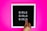 A black letter board with white letters spelling 'GIRLS' repeated three times, set against a bright pink background. A person's hand with neatly manicured nails is adjusting the letters on the board.