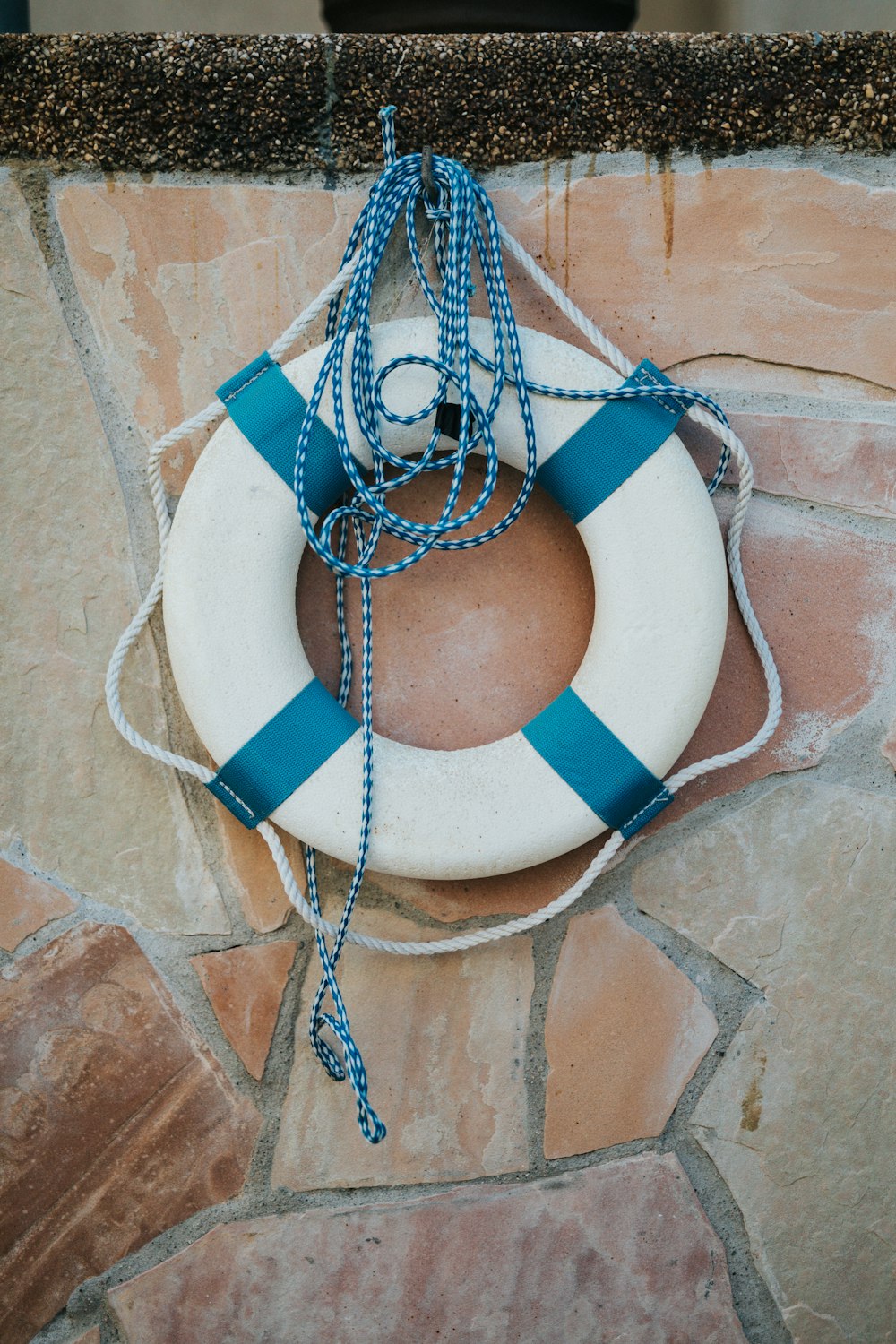 blue and white life buoy on brown concrete wall