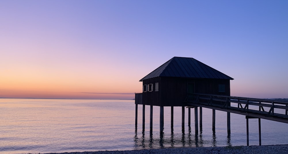 brown wooden house on sea during sunset