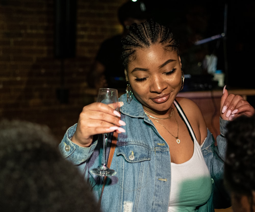 woman in blue denim jacket holding clear drinking glass