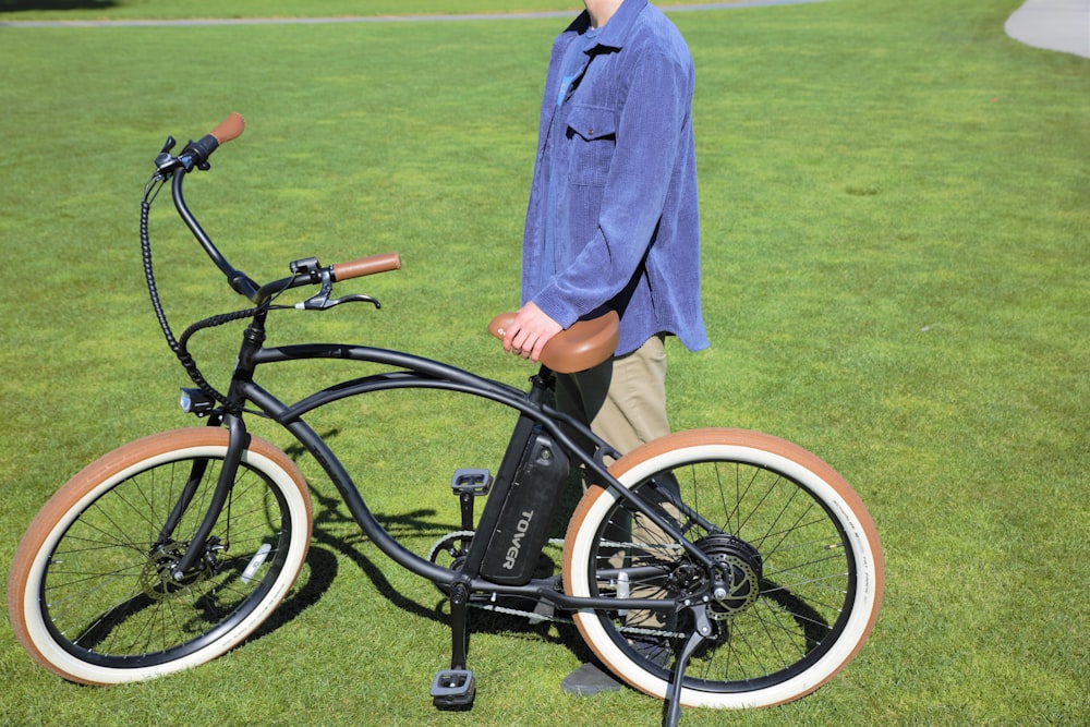 man in blue robe standing beside black bicycle on green grass field during daytime