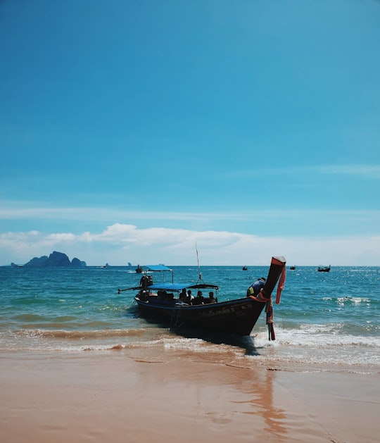 man in red shirt standing on brown wooden boat on sea shore during daytime in Ao Nang Thailand