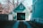 A small, green garage is nestled between two fences and surrounded by bare trees. The structure features vertical siding, a large dark door, and a triangular roof with a small window. Sunlight casts distinct shadows on the building, creating a tranquil suburban scene.