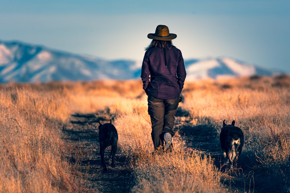 man in brown jacket and brown pants standing beside black short coat dog during daytime